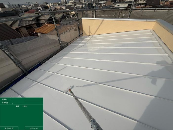 八尾市太子堂のO様邸 金属縦葺き屋根の上塗り作業中 ローラーで白い遮熱塗料を塗り広げている様子